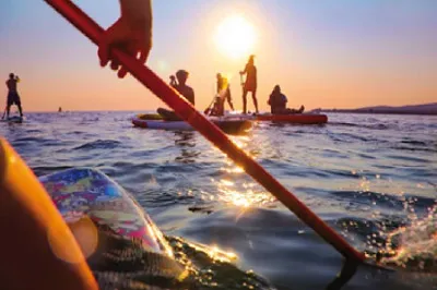 Jugendliche paddeln auf dem Mittelmeer im Sonnenuntergang.